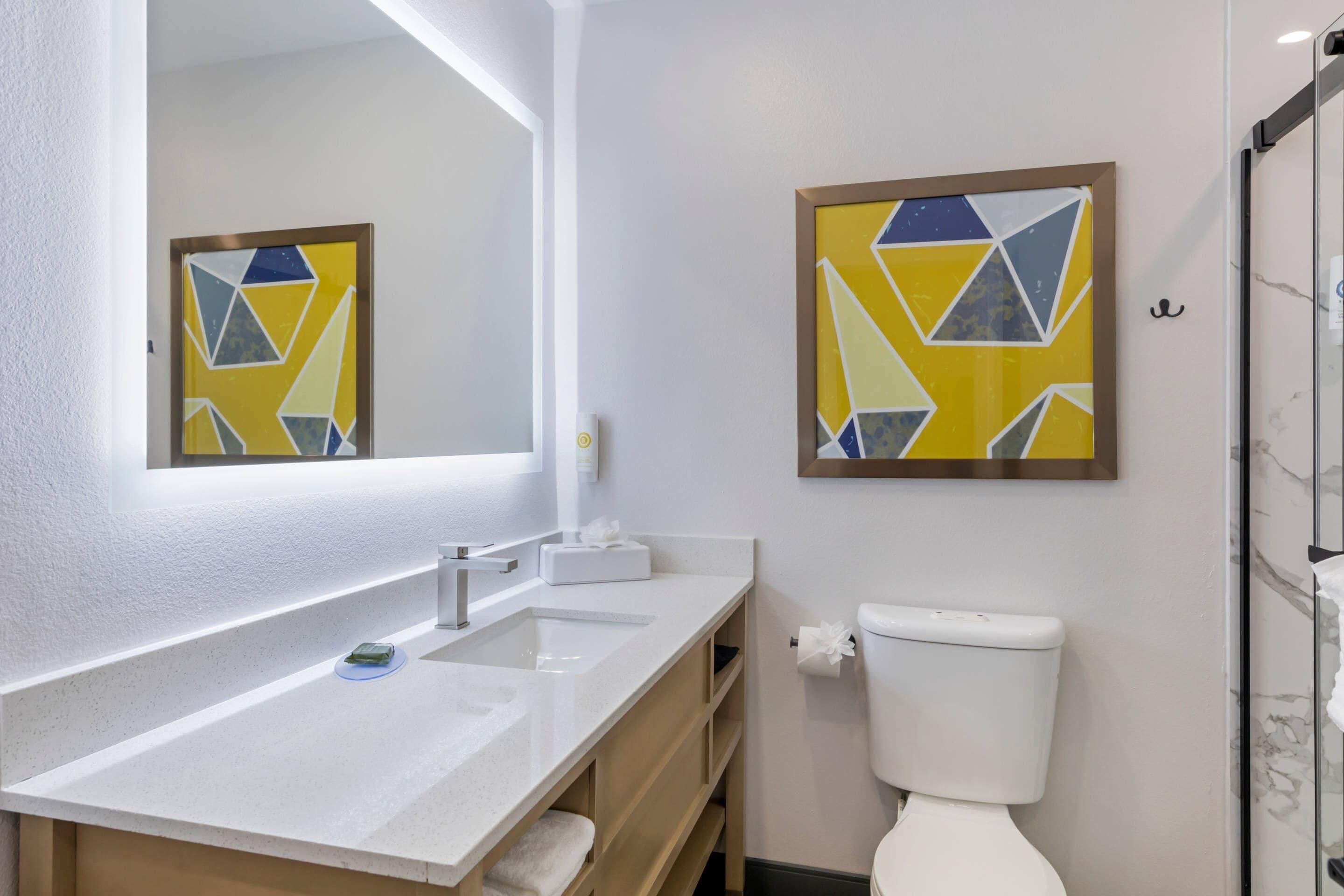 Ein modernes Badezimmer mit einem weißen Waschbecken, einer Toilette und zwei geometrischen Kunstwerken an der Wand.