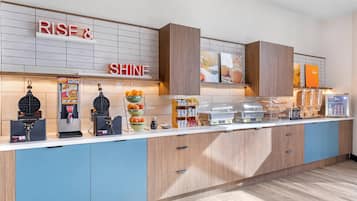 Un bar à petit-déjeuner équipé d’un appareil à gaufres, d’une machine à café et d’un panier de fruits.
