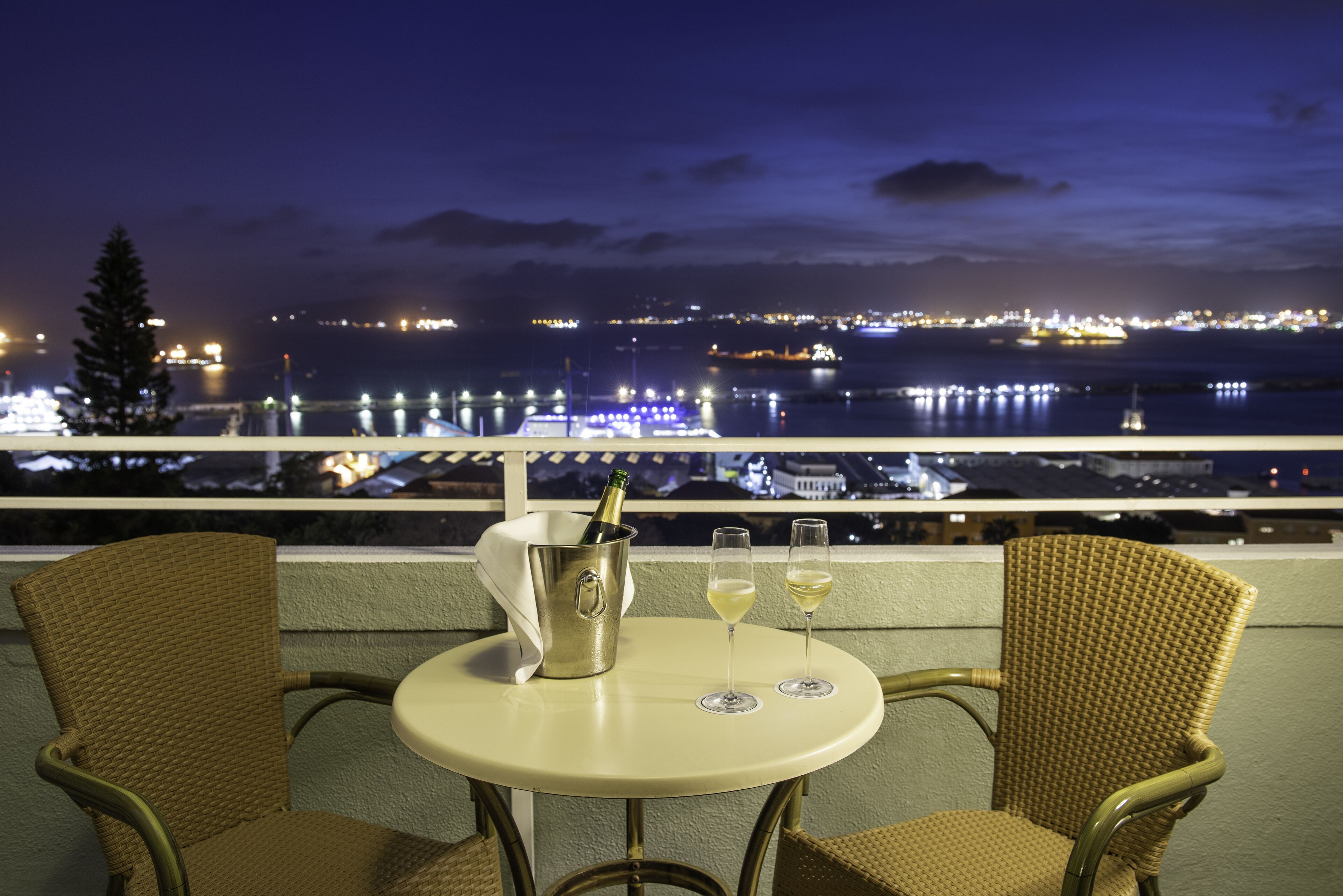 Un balcon avec des fauteuils en osier, une table et un seau à champagne contenant deux verres de vin.