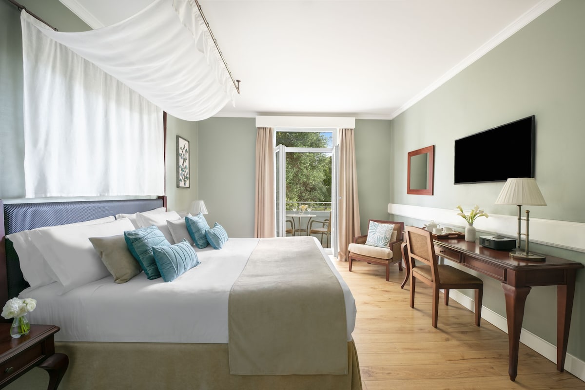 A hotel room with a large bed, a desk with a lamp, a chair, and a TV.