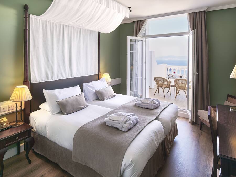 Ein Hotelzimmer mit einem großen Bett, Nachttischlampen, einem Telefon und einem Balkon mit Sitzgelegenheiten.