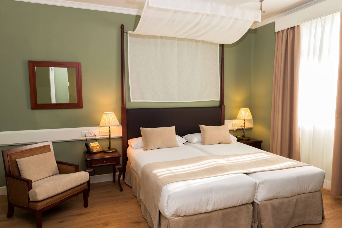 A hotel room with a large bed, two bedside tables with lamps, a chair, a mirror, and a canopy bed.