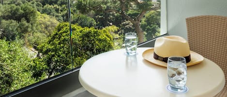 Un balcon avec une table, une chaise en osier, un chapeau et un verre d’eau.