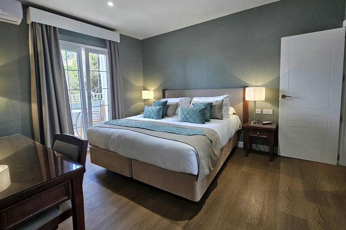 A hotel room with a large bed, bedside lamps, a desk, and a door.