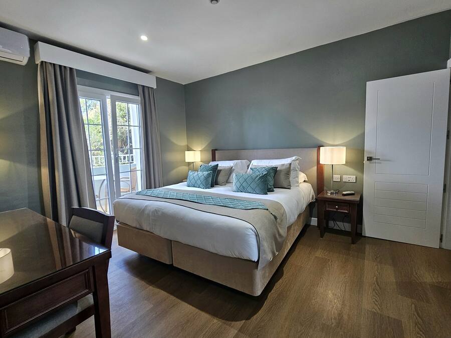 Una habitación de hotel con una cama grande, lámparas de noche, un escritorio y una puerta.