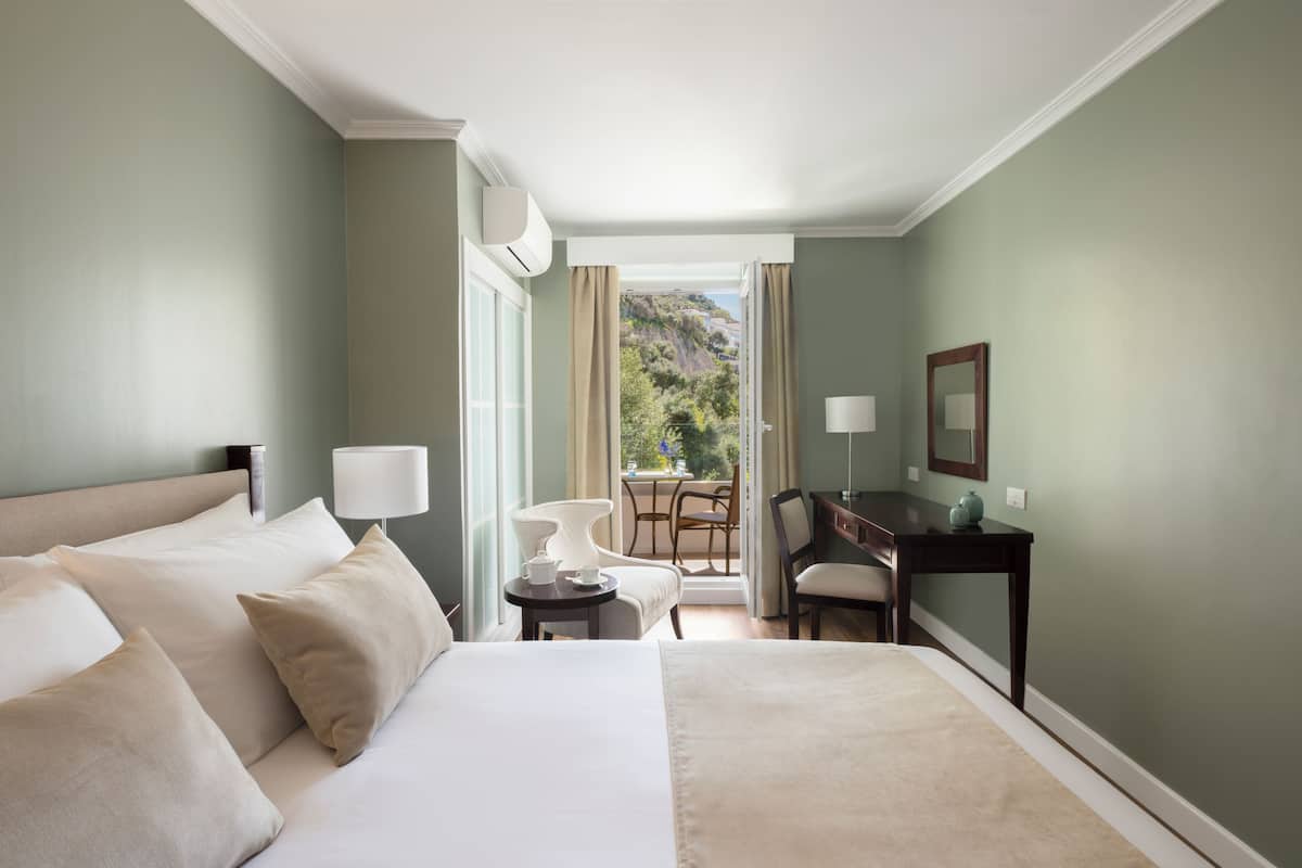 A hotel room with a large bed, a desk, a chair, and a view of the outdoors.