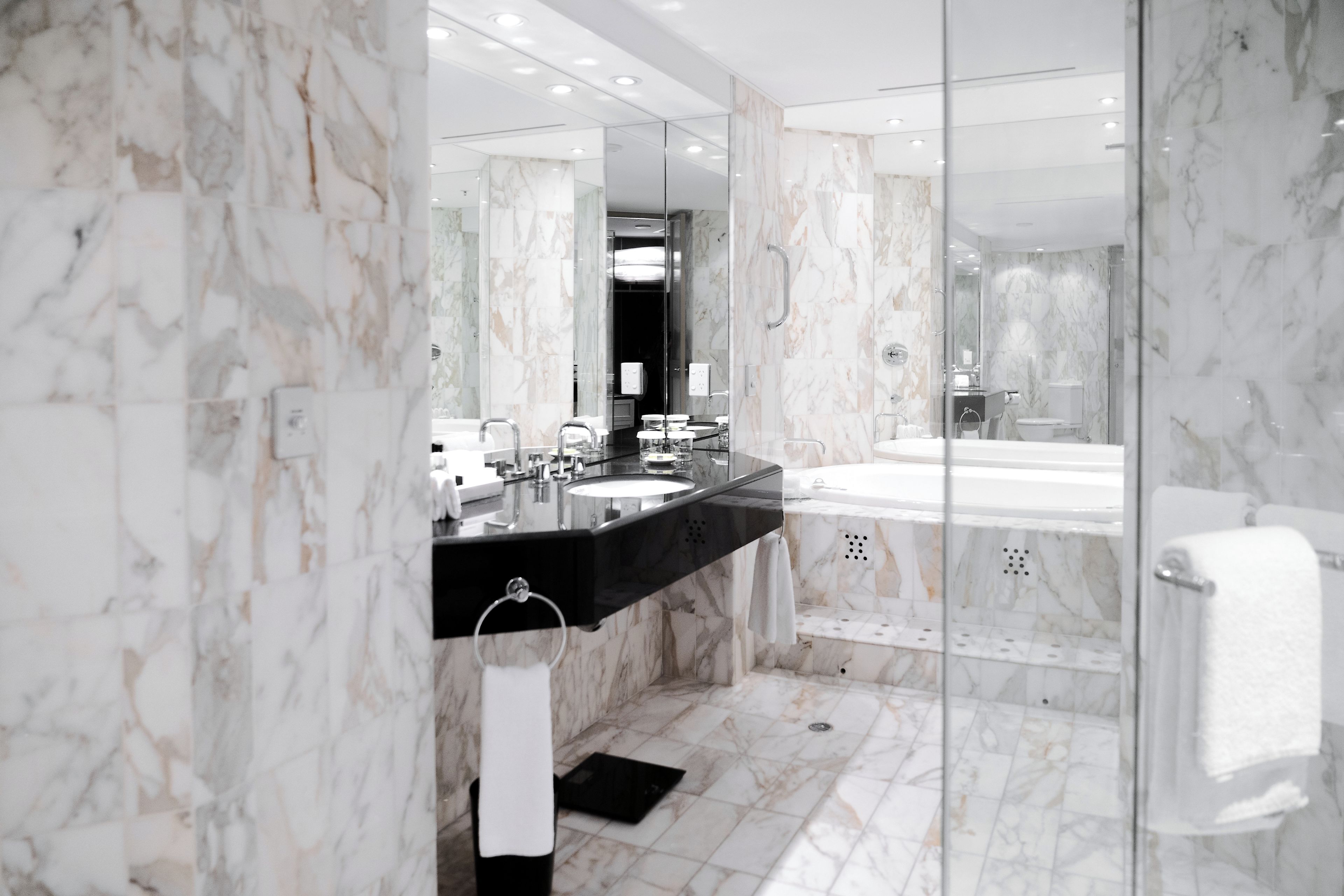 A modern bathroom with a marble floor, a black countertop sink, a large mirror, and a glass-enclosed shower area.
