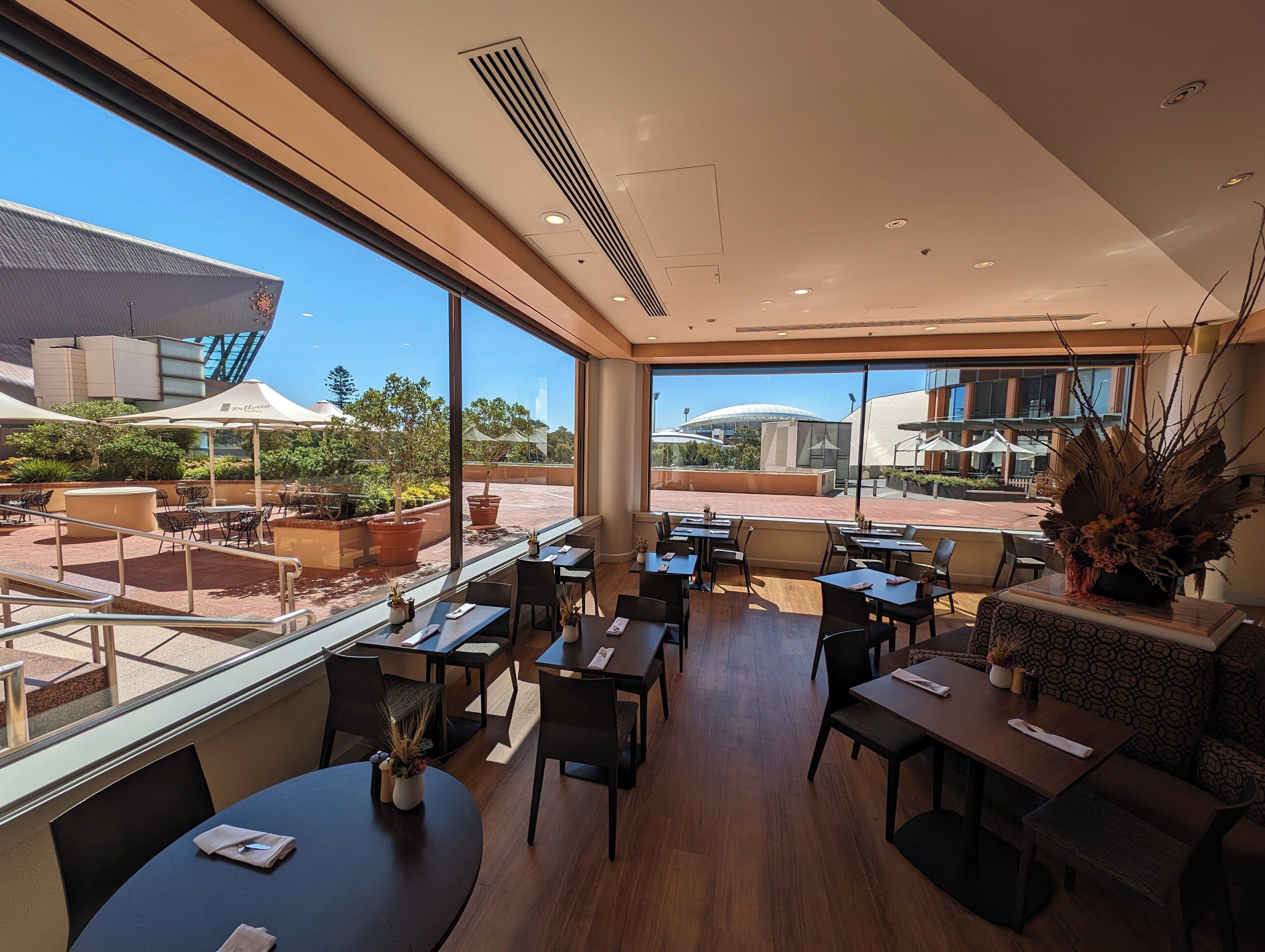 A modern dining area with tables and chairs, large windows offering views of the outdoor seating area and a building with a dome structure.