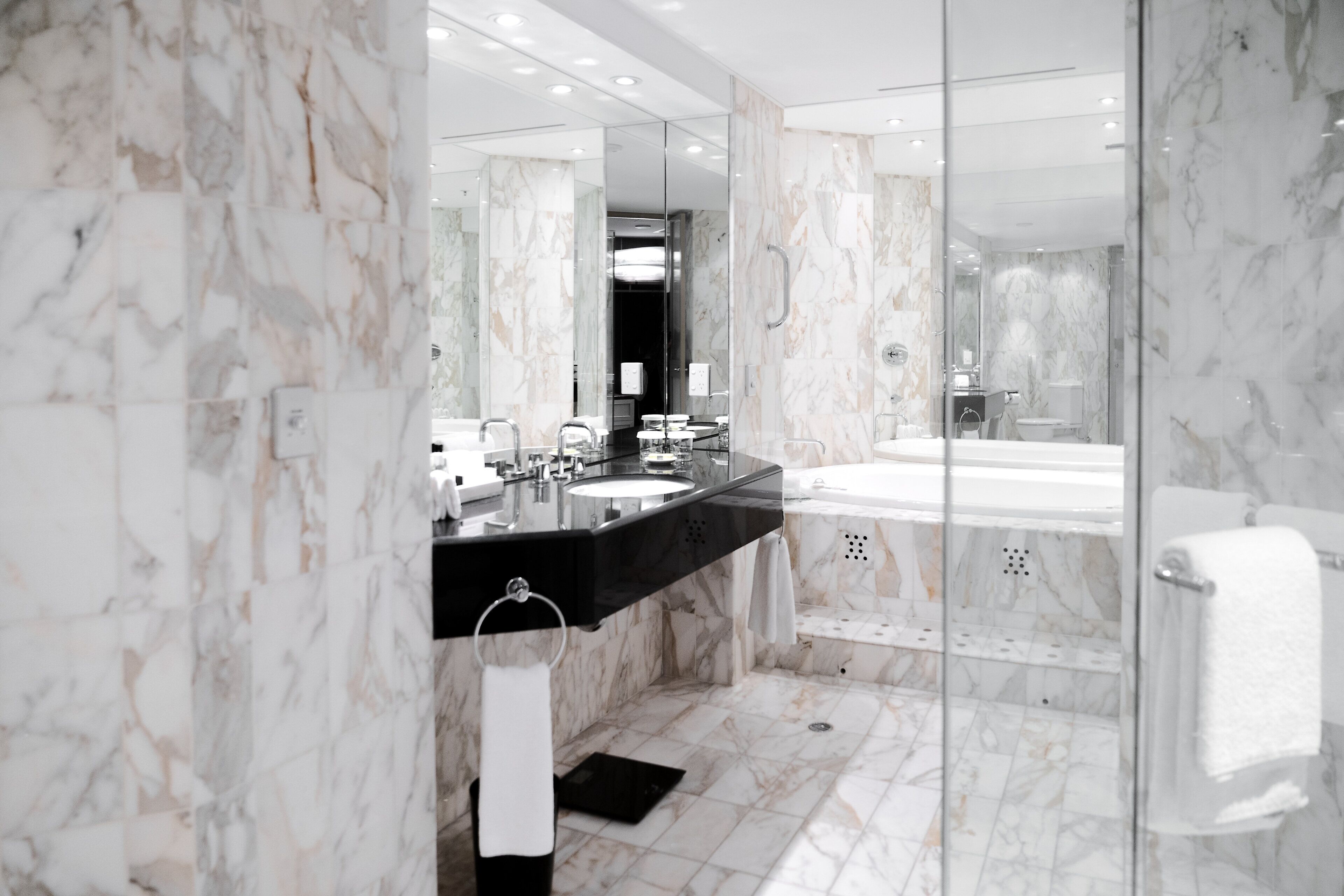 A modern bathroom with a marble floor, a black sink, a large mirror, and a glass-enclosed shower area.