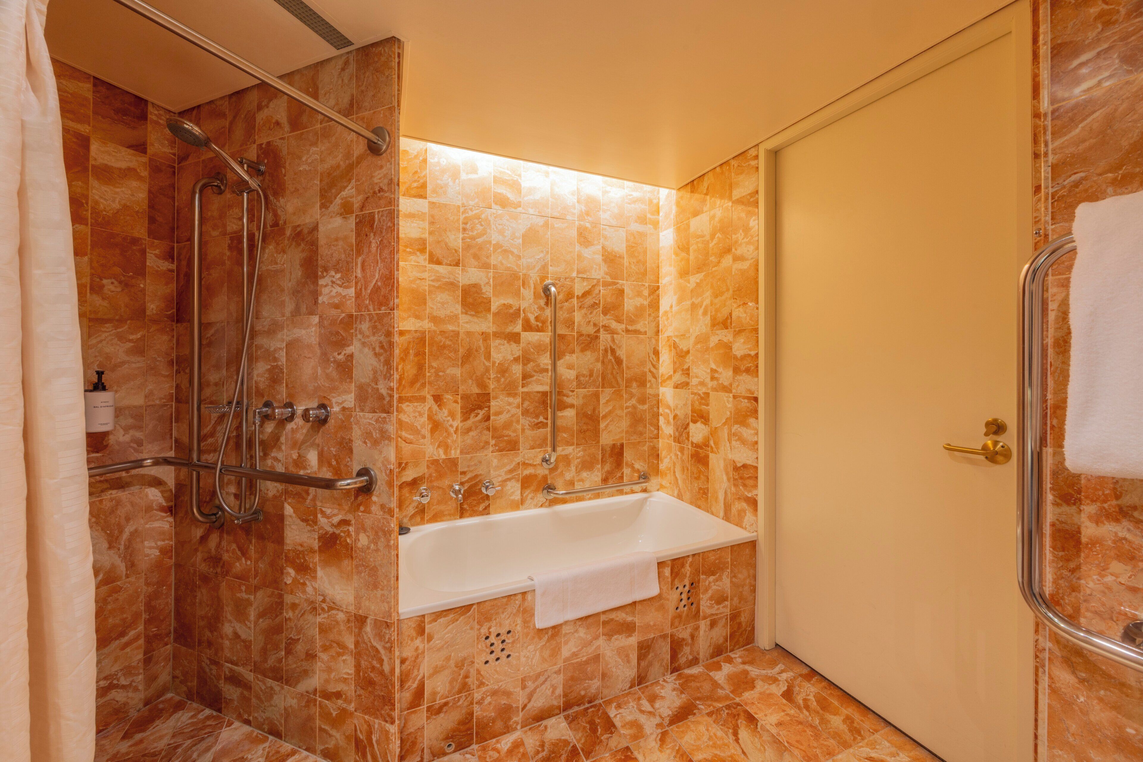 A bathroom with a shower, grab bars, a white sink, and a door with a towel hanging on the handle.