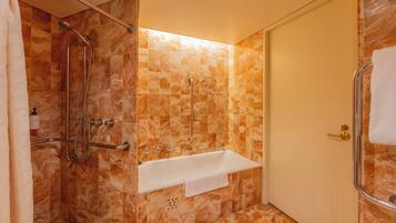 A bathroom with a shower, grab bars, a white sink, and a door with a towel hanging on the handle.