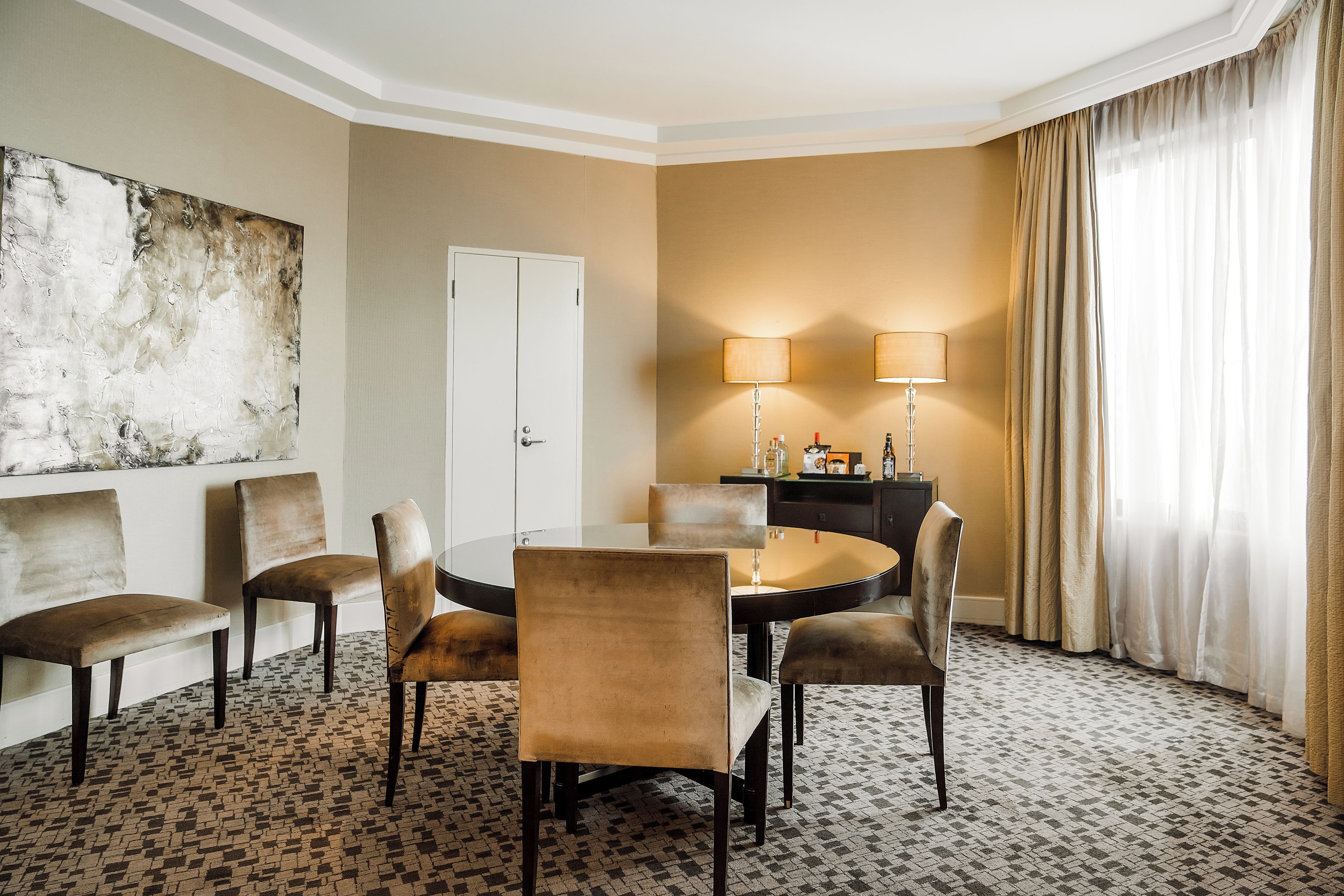 Habitación de hotel con una mesa redonda, cuatro sillas, un sofá, una lámpara y un cuadro en la pared.