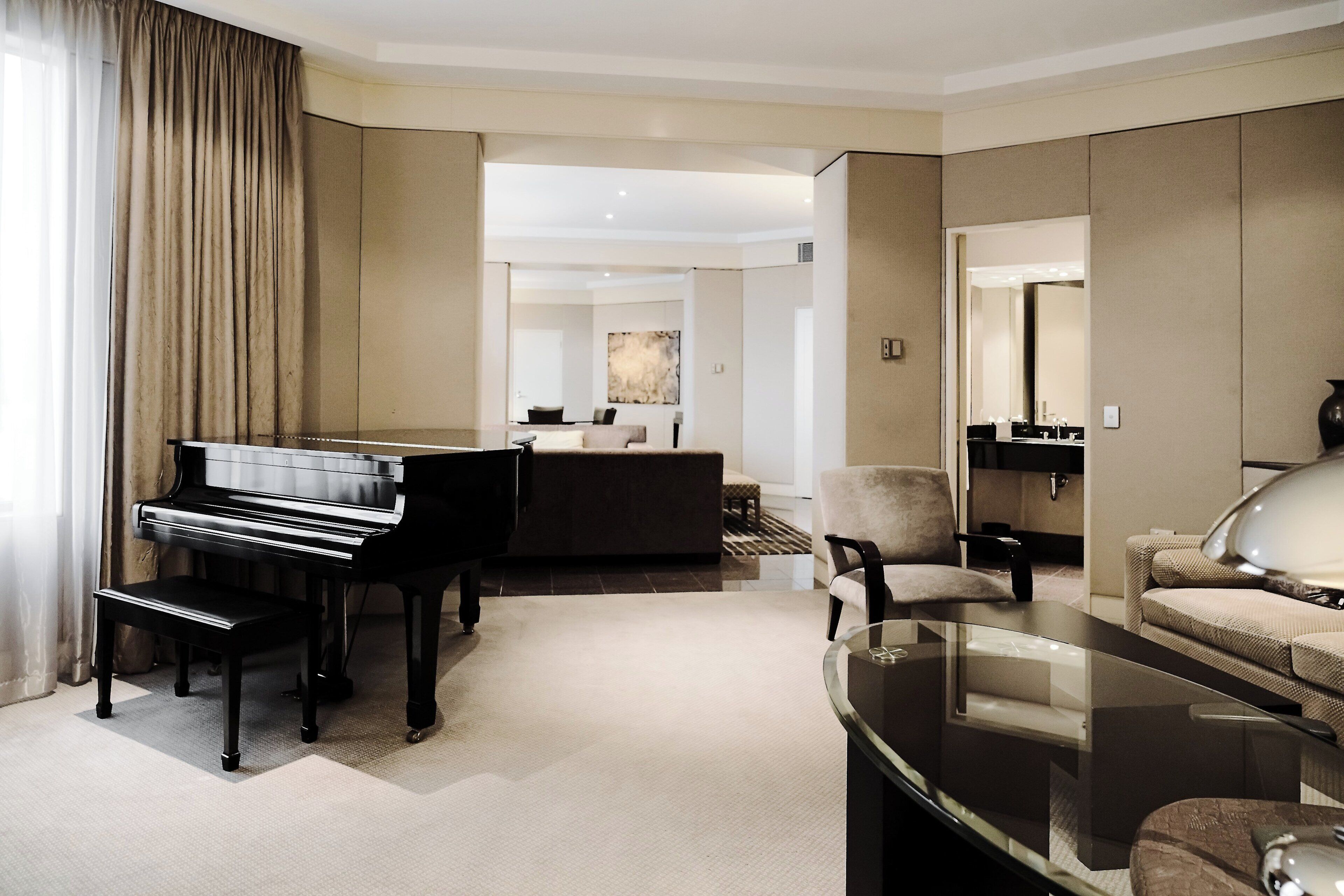 A modern hotel room with a piano, a glass coffee table, a sofa, and a large mirror.