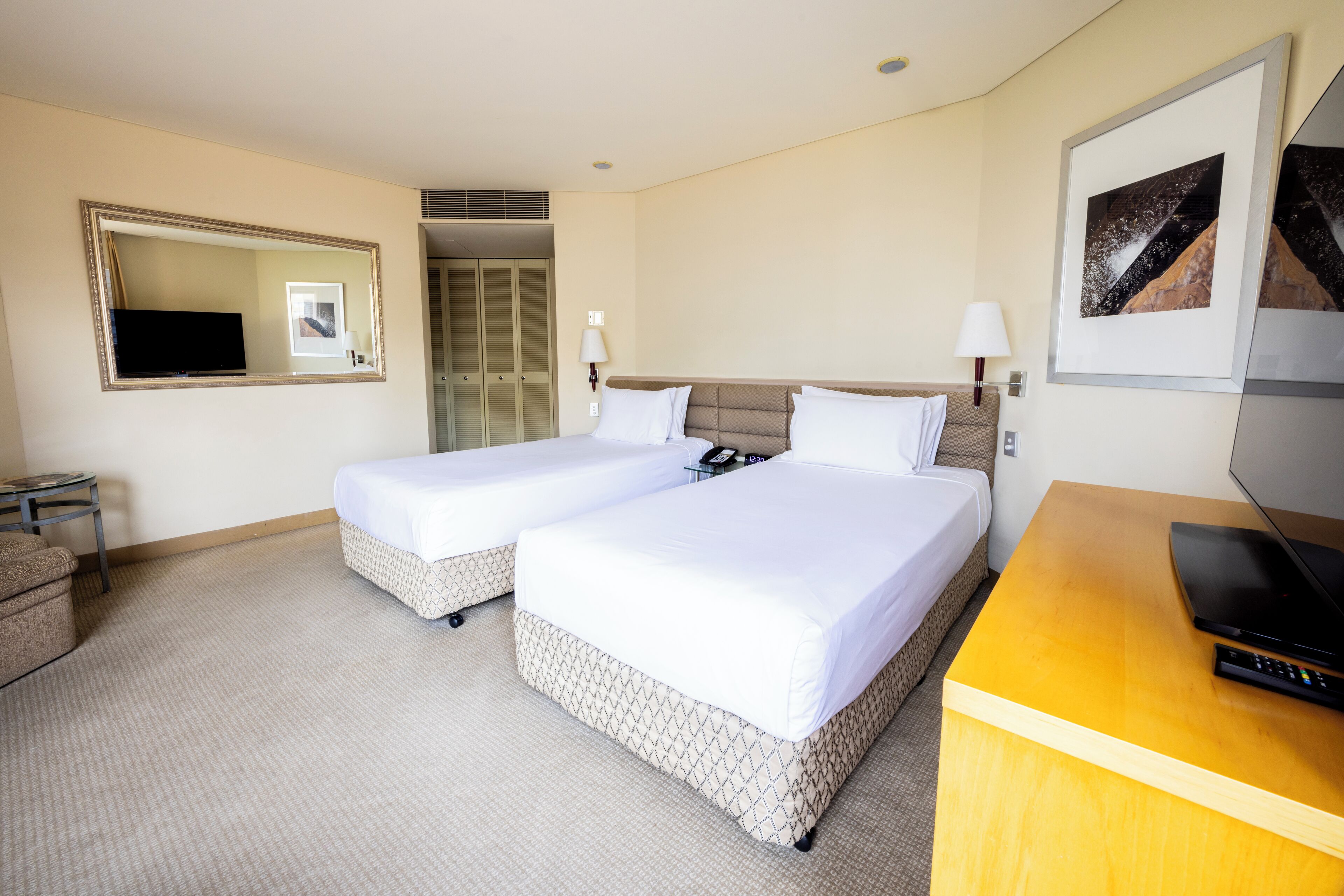 A hotel room with two beds, a TV, a desk, and a mirror.