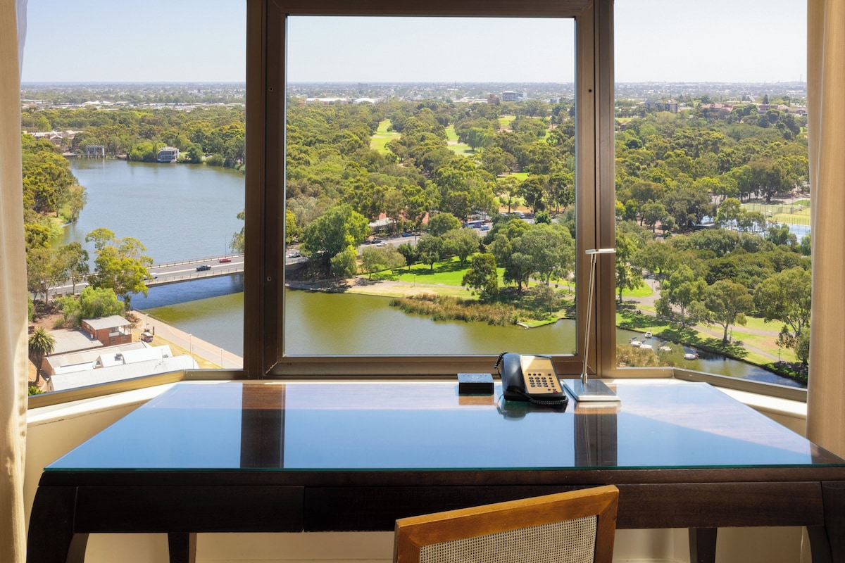 A room with a large window offering a view of a lake and surrounding greenery.