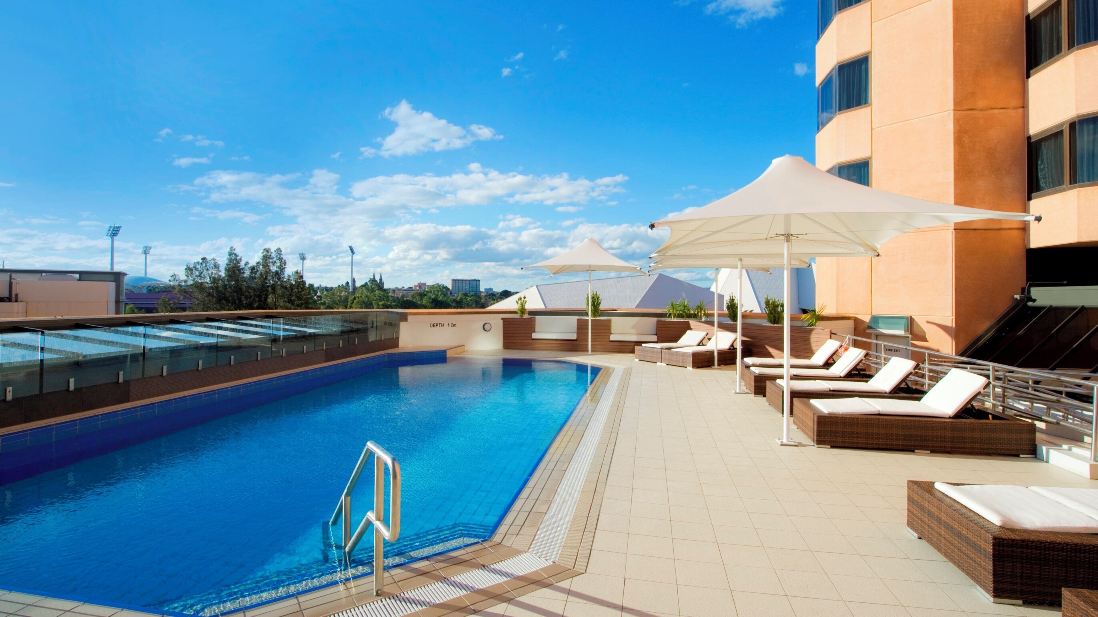 A rooftop swimming pool with lounge chairs and umbrellas, surrounded by a modern building.