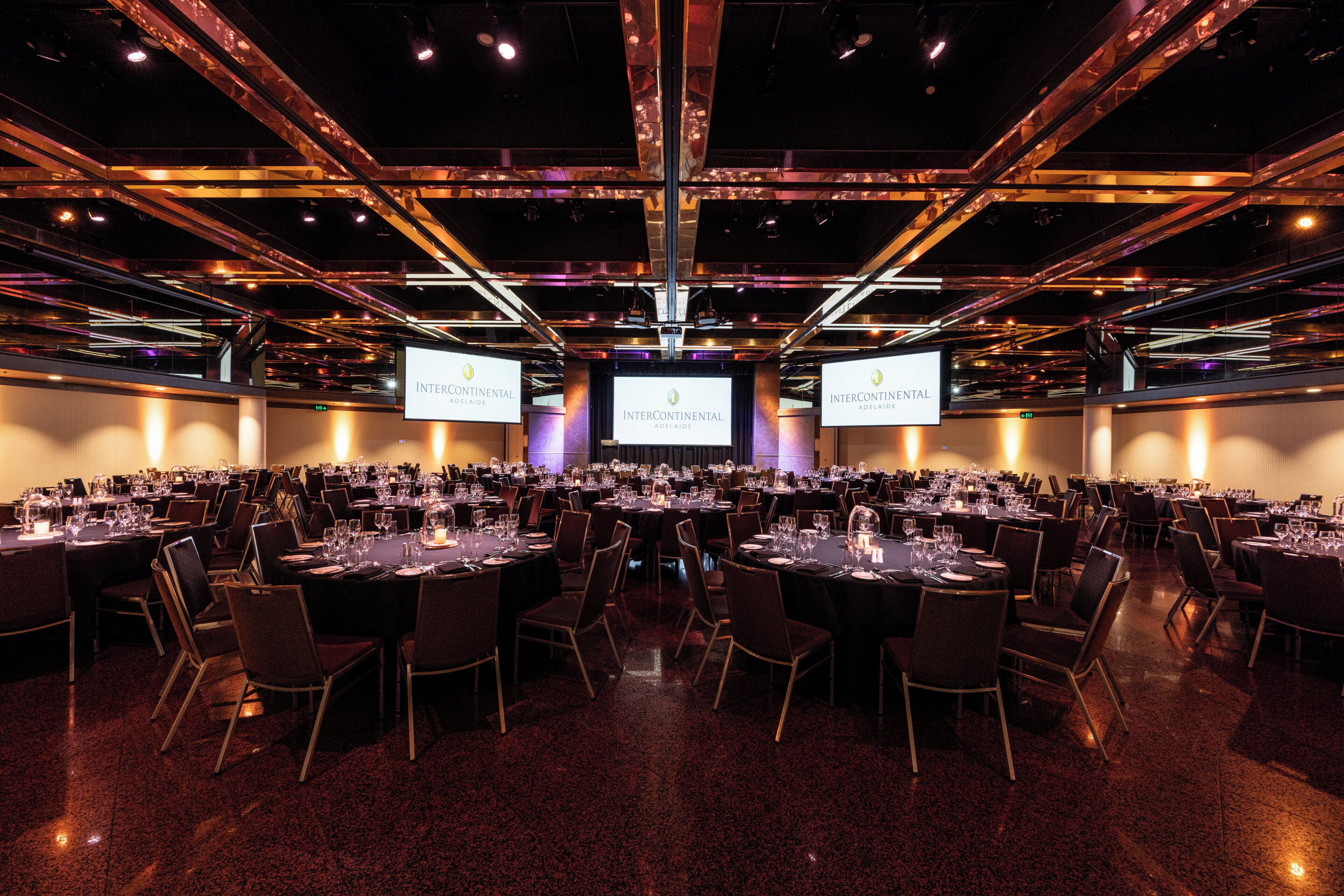 A conference room with multiple tables, chairs, and large screens displaying 'Intercontinental Adelaide'.