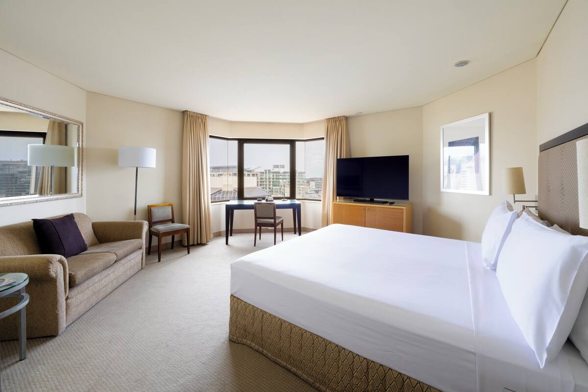 Habitación de hotel con una cama grande, un escritorio con silla, televisión y vistas a la ciudad.