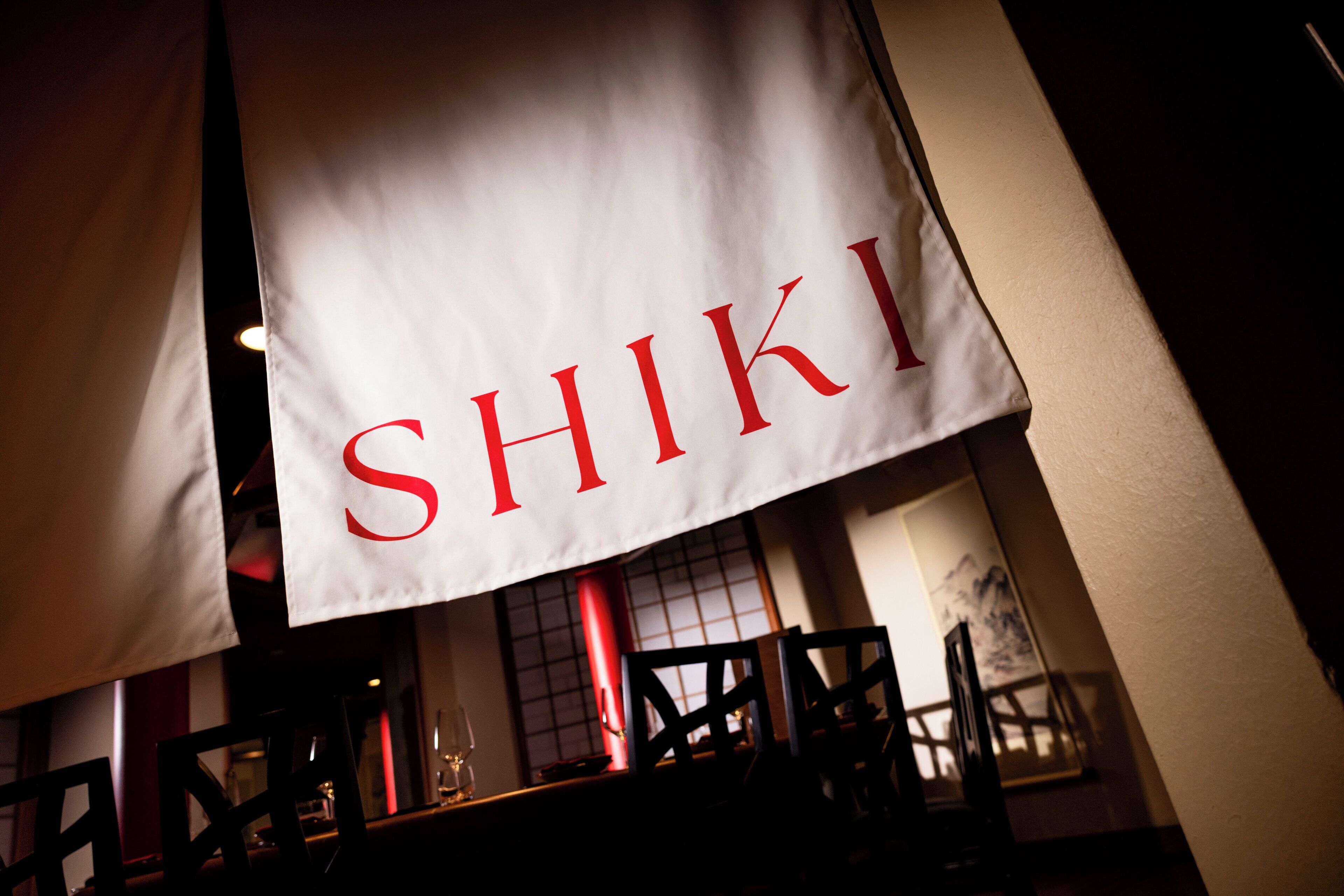 Interior de un restaurante con un cartel que muestra la palabra 'SHIKI' en letras rojas.