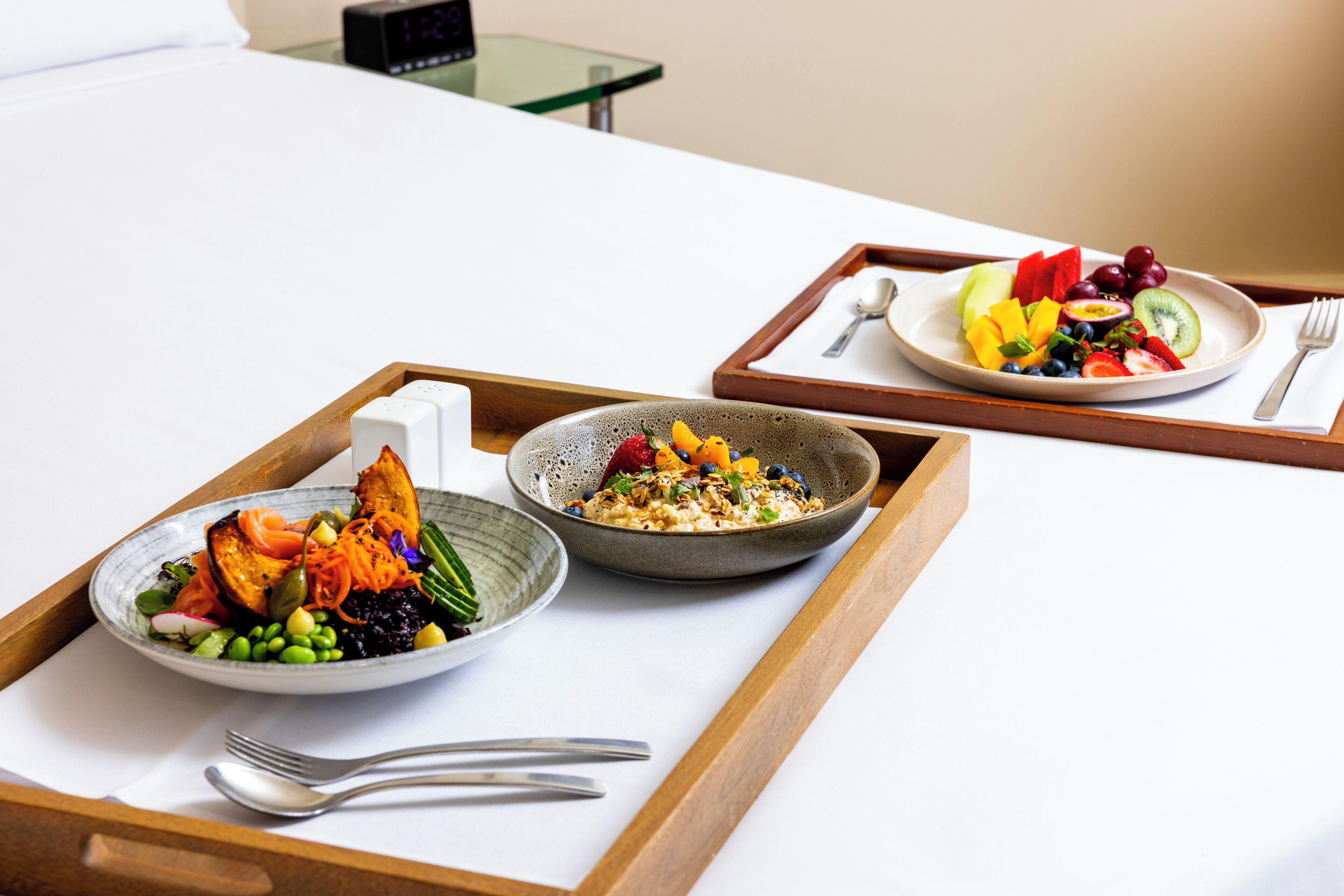 A breakfast tray with two bowls of food, a spoon, and a fork on a bed.