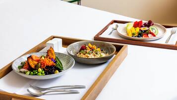 A breakfast tray with two bowls of food, a spoon, and a fork on a bed.