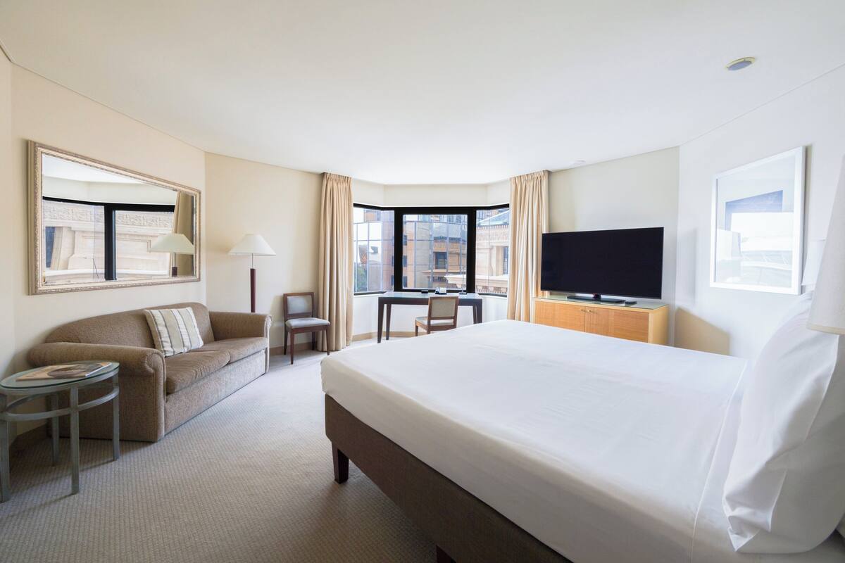 Habitación de hotel con una cama grande, un escritorio, una silla, un televisor y una ventana con cortinas.