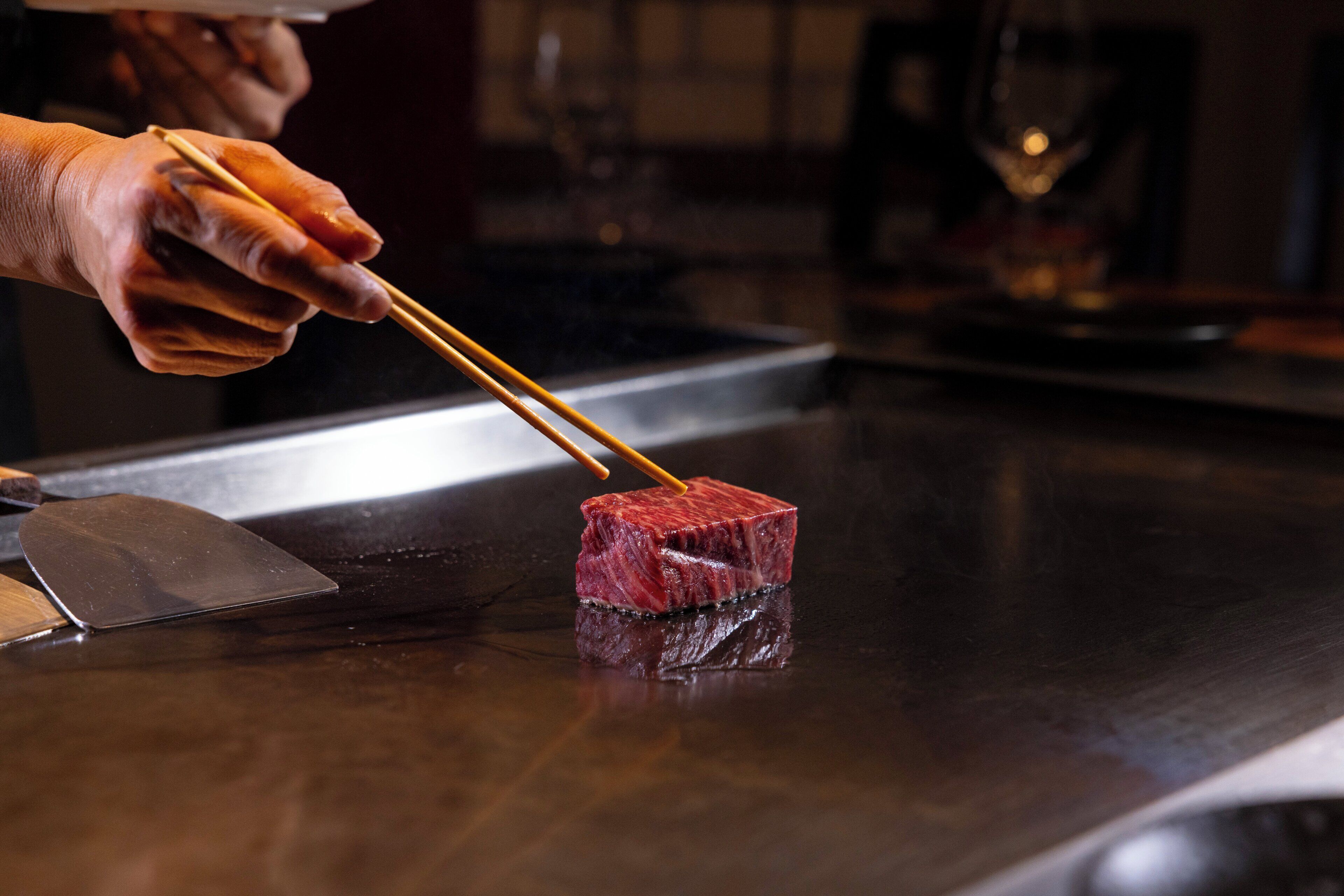 A person using chopsticks to handle a piece of meat on a dark countertop.