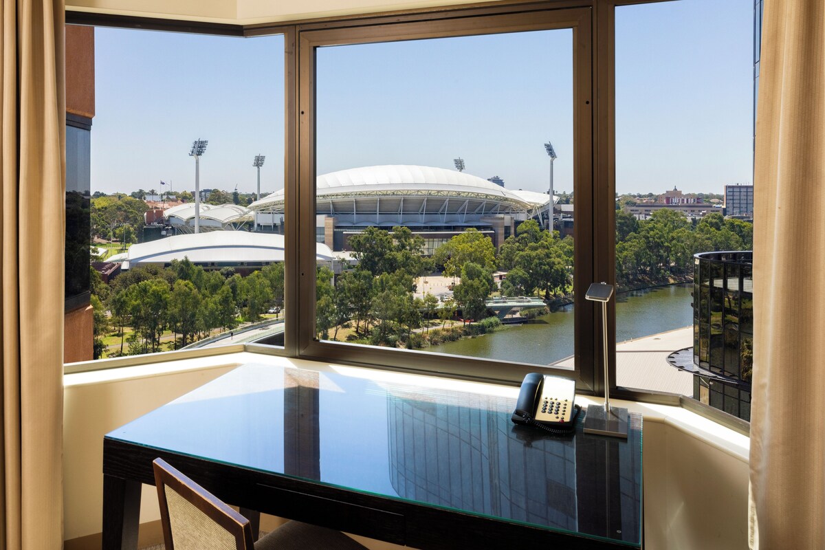 A hotel room with a large window offering a view of a stadium and a river.