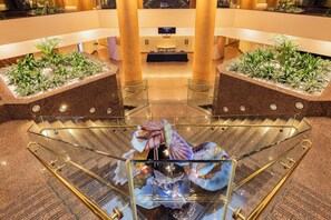 A hotel lobby with a glass elevator, a reception desk, and decorative plants.