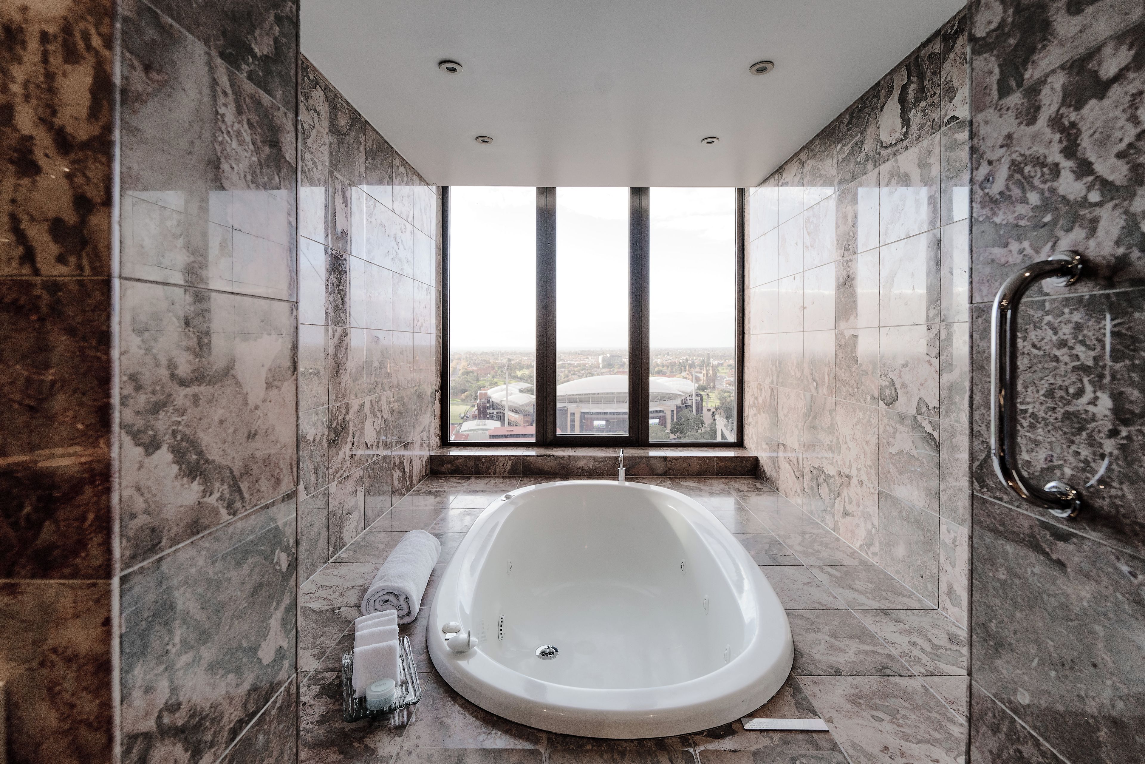 A modern bathroom with a freestanding bathtub, a handrail, and a window offering a city view.