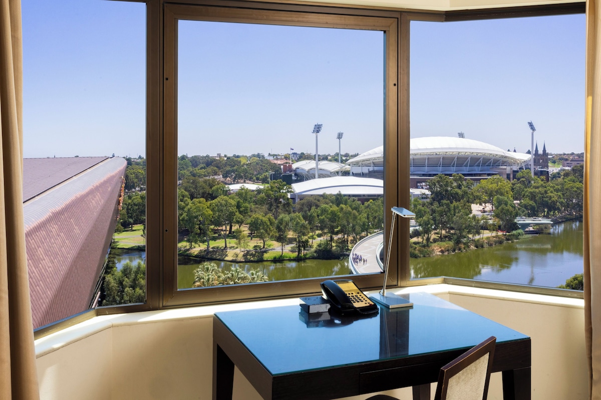 A room with a large window offering a view of a stadium and a lake.
