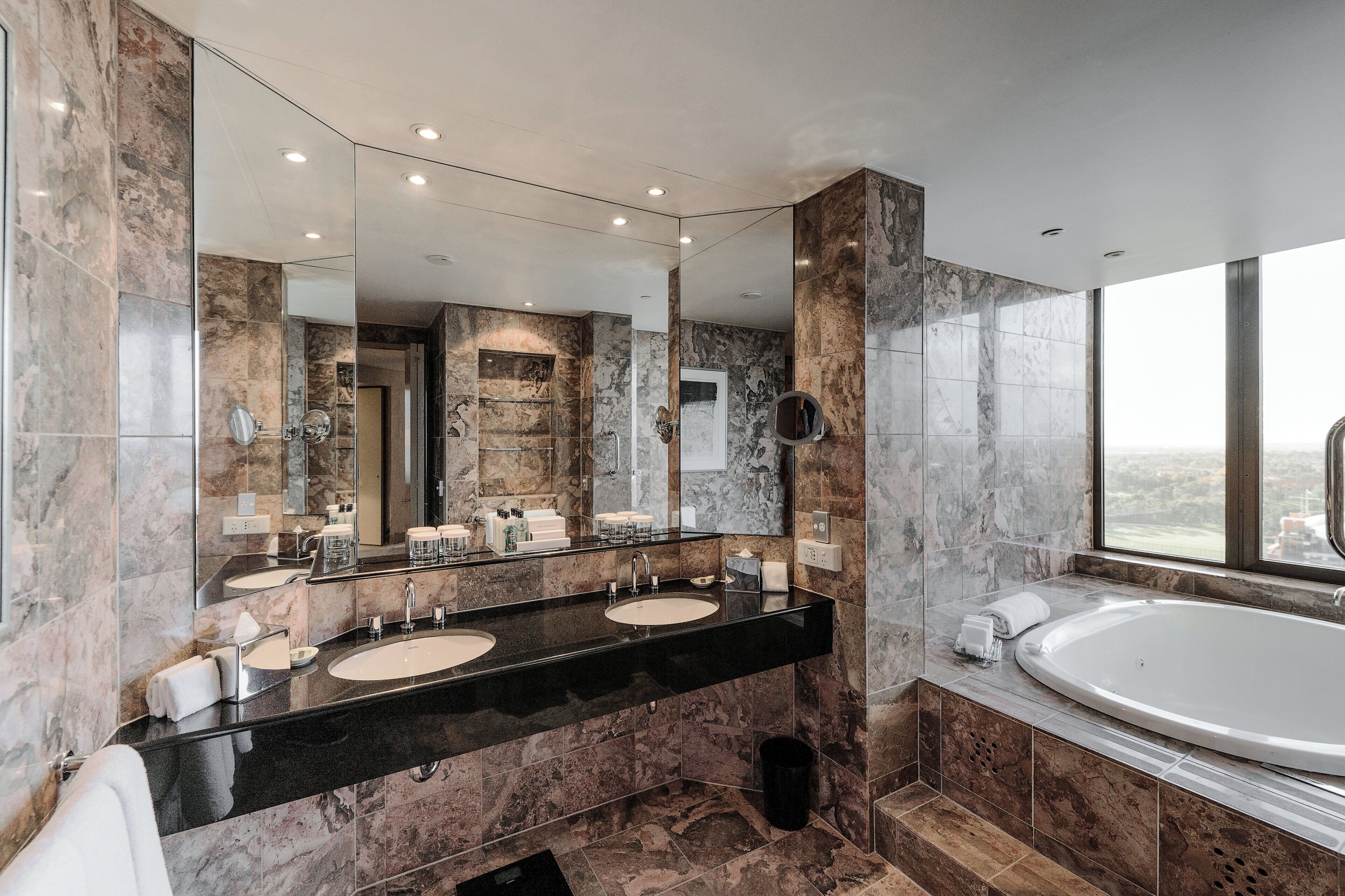 A modern bathroom with two sinks, a large mirror, and a bathtub.