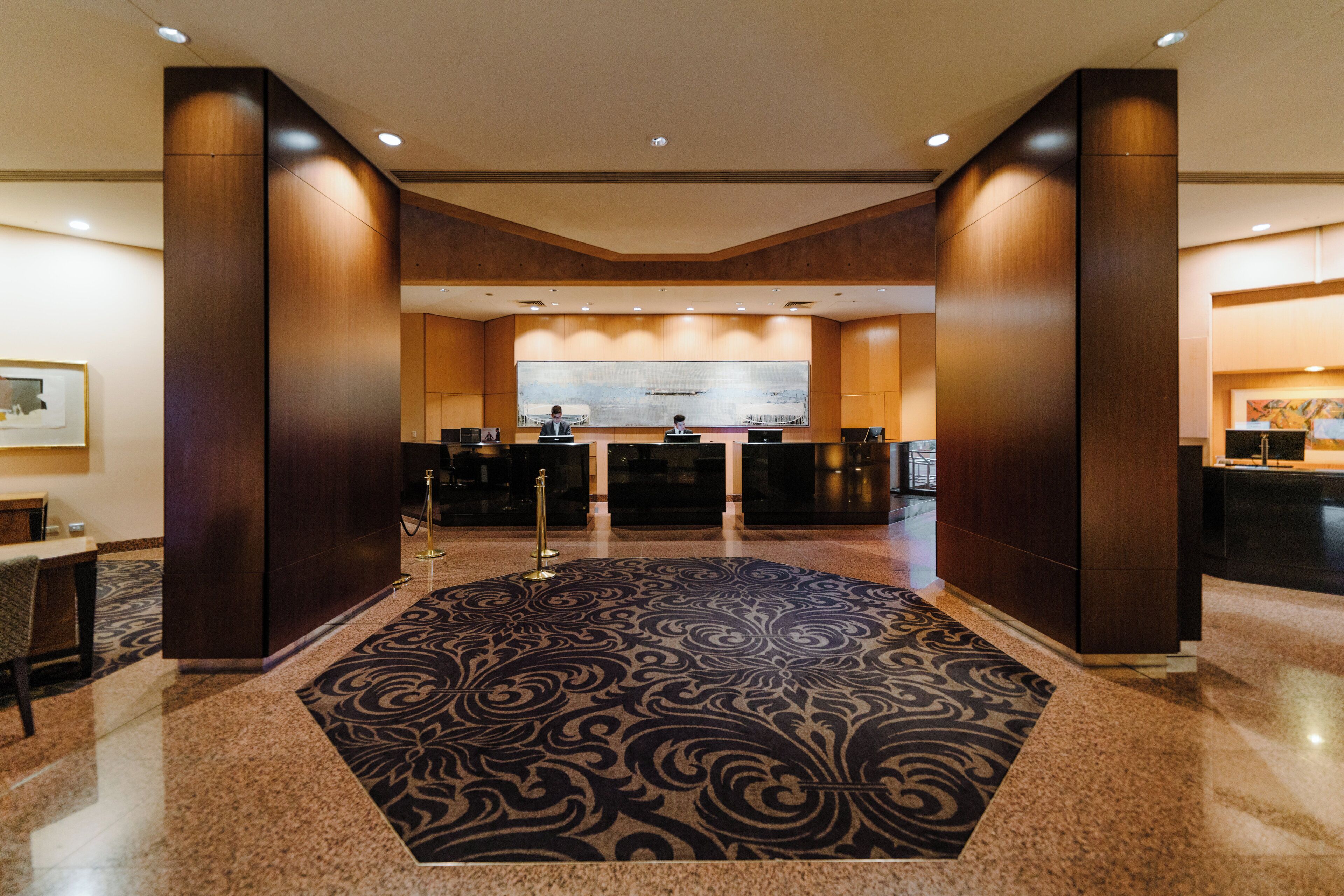 A hotel lobby with a reception desk, a large abstract painting, and a patterned carpet.