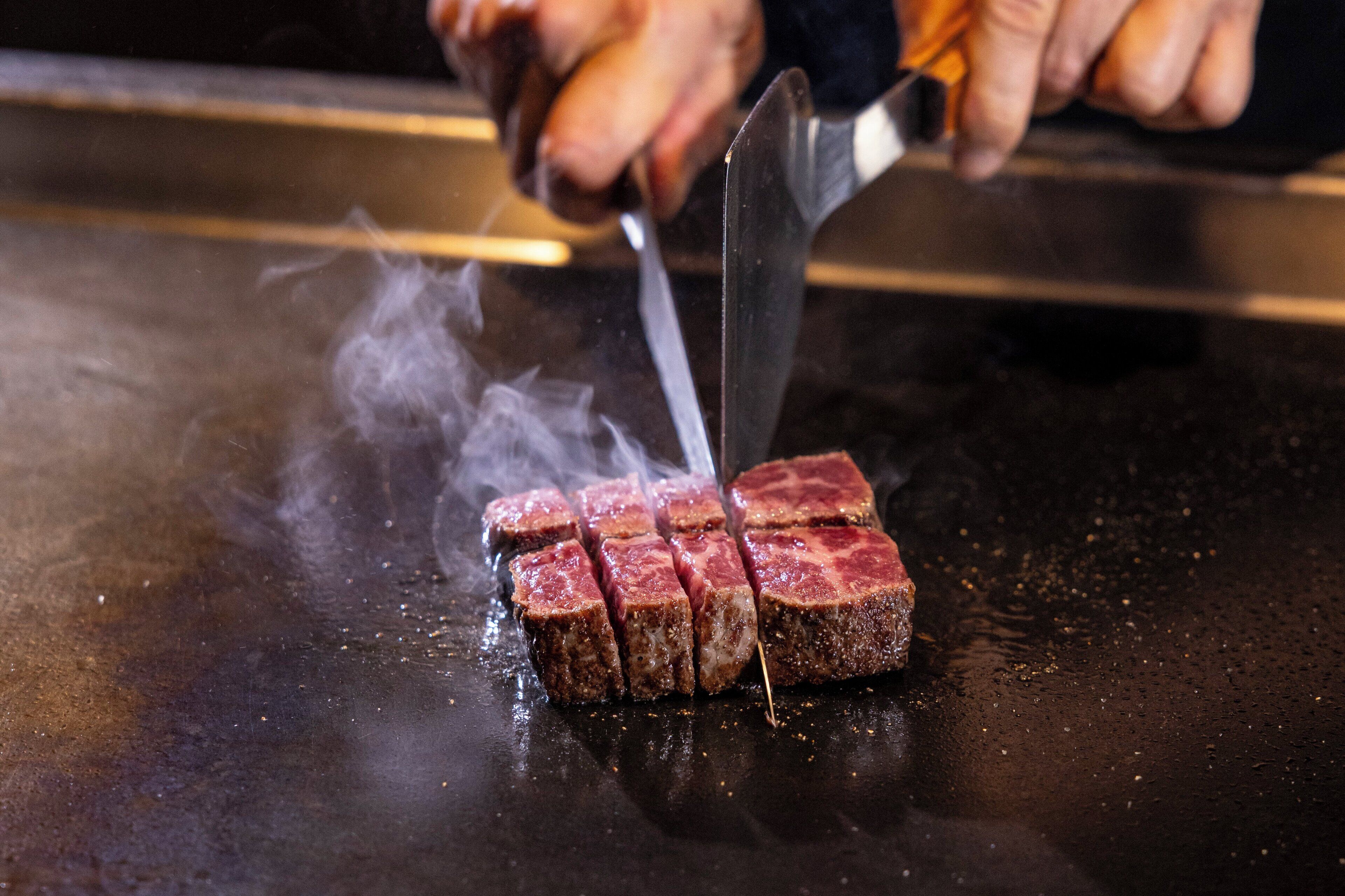 Un bistec siendo cortado sobre una parrilla.