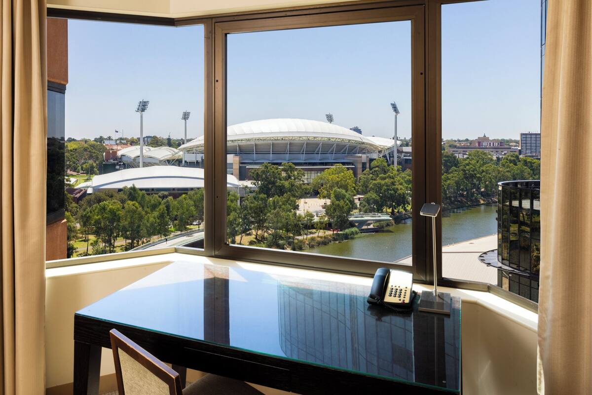 Una habitación de hotel con un ventanal que ofrece vistas a un estadio y un río.