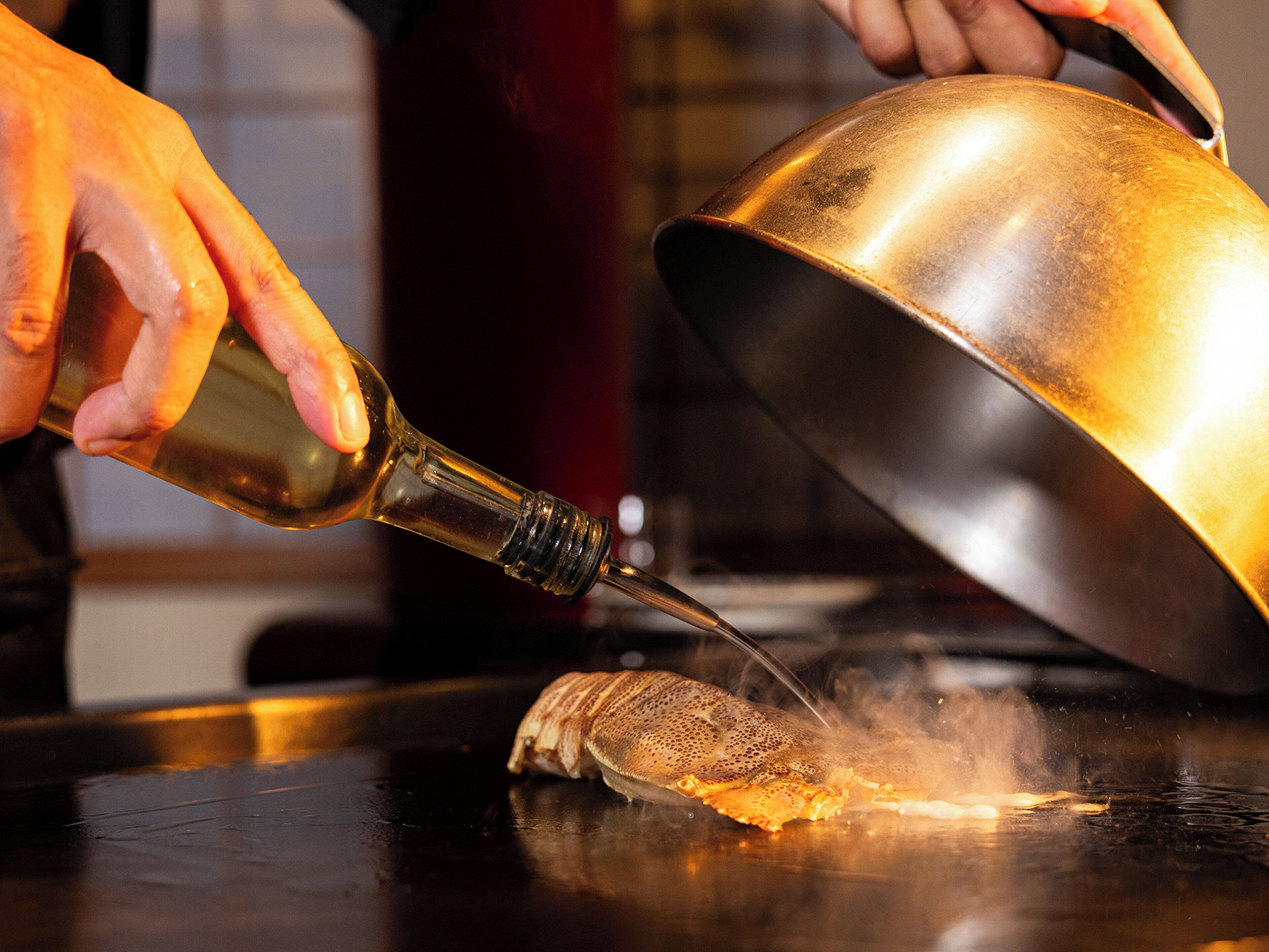 A person pouring a liquid from a bottle into a large metal bowl on a table.