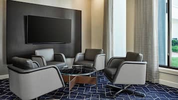 A conference room with a large flat-screen TV, four grey chairs, a glass coffee table, and a patterned carpet.