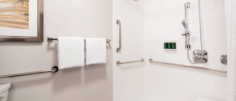 A modern bathroom with a shower, grab bars, a toilet, and a framed artwork on the wall.