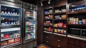 Un refrigerador bien surtido con bebidas, estantes con aperitivos y un microondas en un entorno comercial.