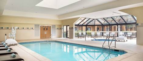 A swimming pool with sunroof and lounge chairs, surrounded by a tiled floor and a view of the outdoors.