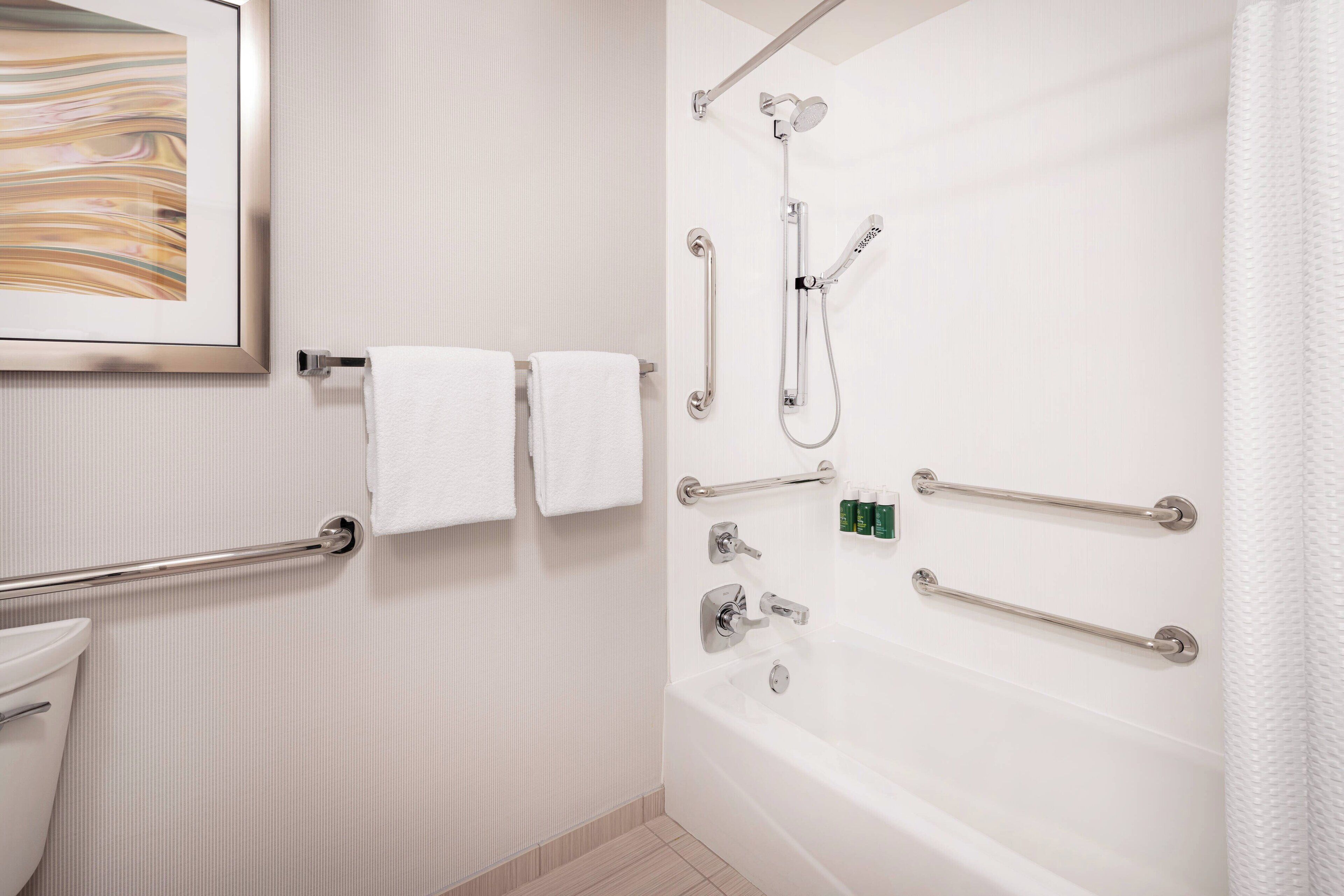 A bathroom with a bathtub, a shower, and handrails. There are two towels hanging on a rack.