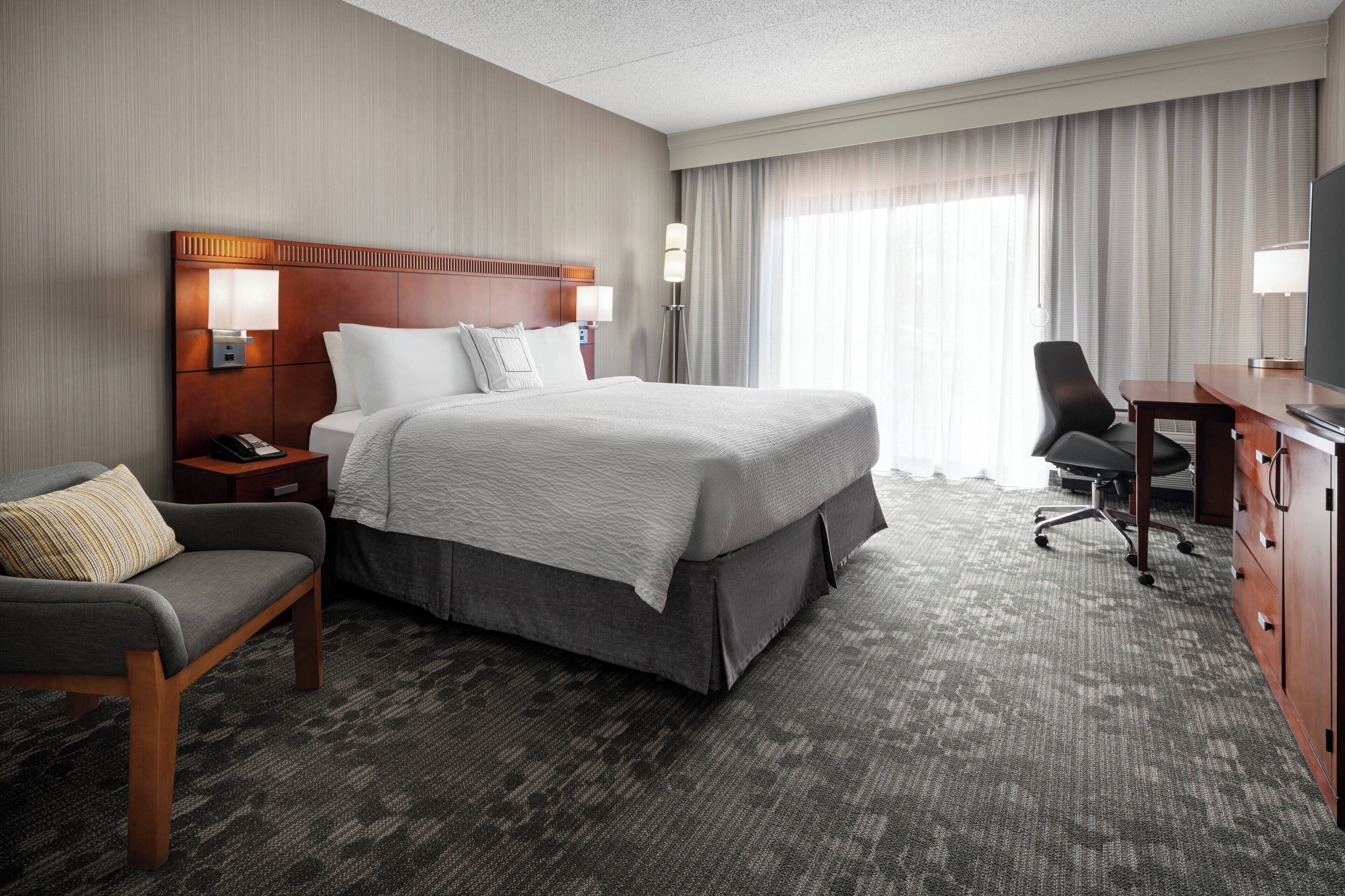 Ein Hotelzimmer mit einem großen Bett, einem Schreibtisch, einem Sessel, einem Nachttisch und einem Fernseher.
