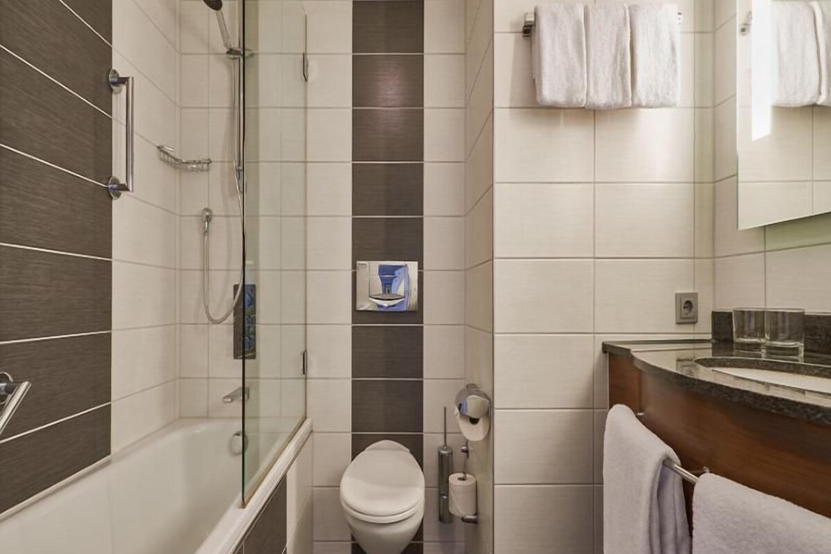 A bathroom with a glass-enclosed shower, a toilet, and a sink with a towel rack.