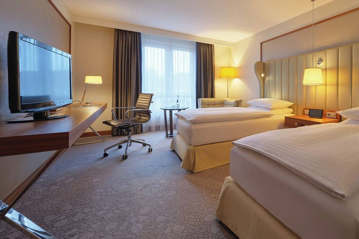 A hotel room with two beds, a desk with a television, a chair, and a lamp.