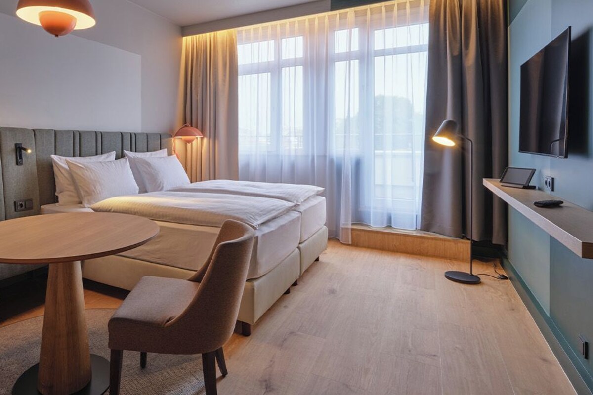 A hotel room with a bed, a sofa, a round table, two chairs, a TV, and a desk with a computer.