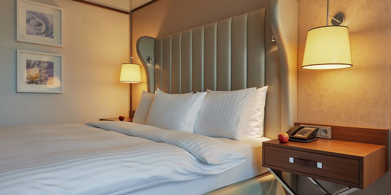 A hotel room with a bed, bedside lamps, a bedside table with a telephone, and framed pictures on the wall.