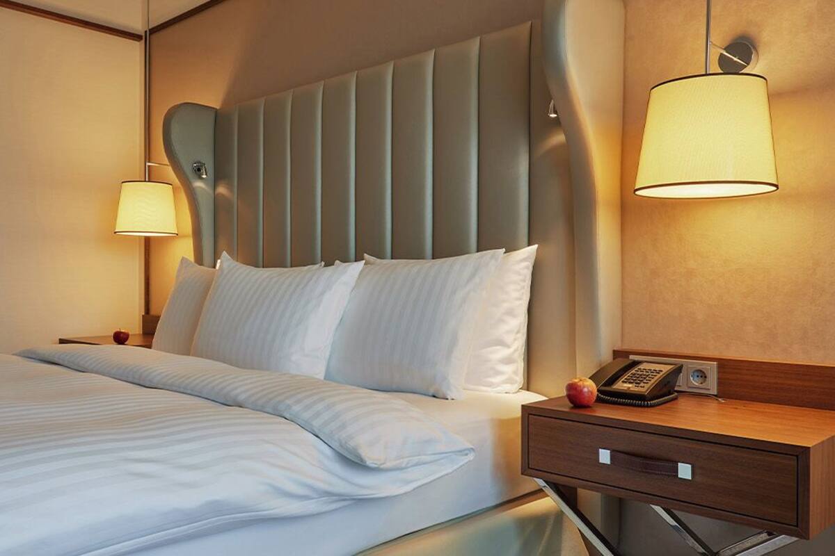 A hotel room with a bed, bedside lamps, a bedside table with a telephone, and framed pictures on the wall.