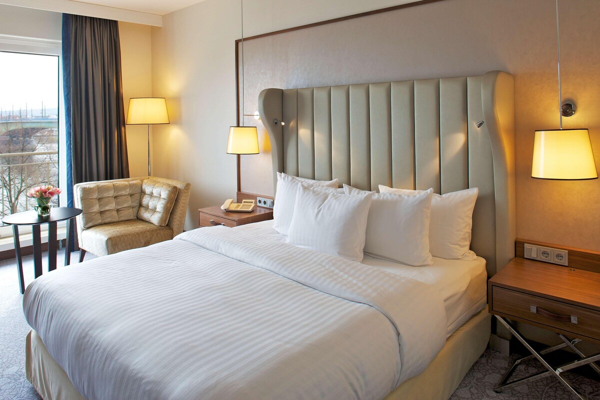 A hotel room with a large bed, a chair, a nightstand, and a lamp.