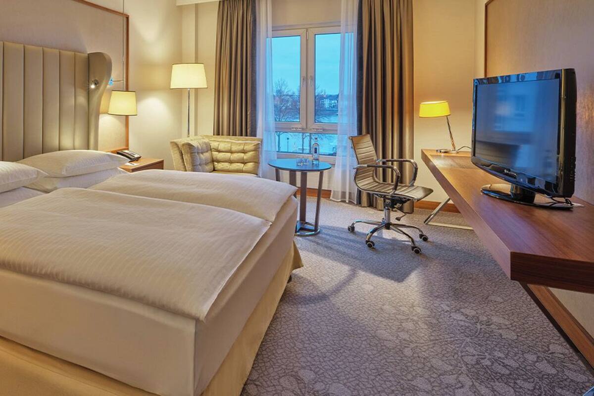 A hotel room with a large bed, a desk with a television, a chair, and a small table.