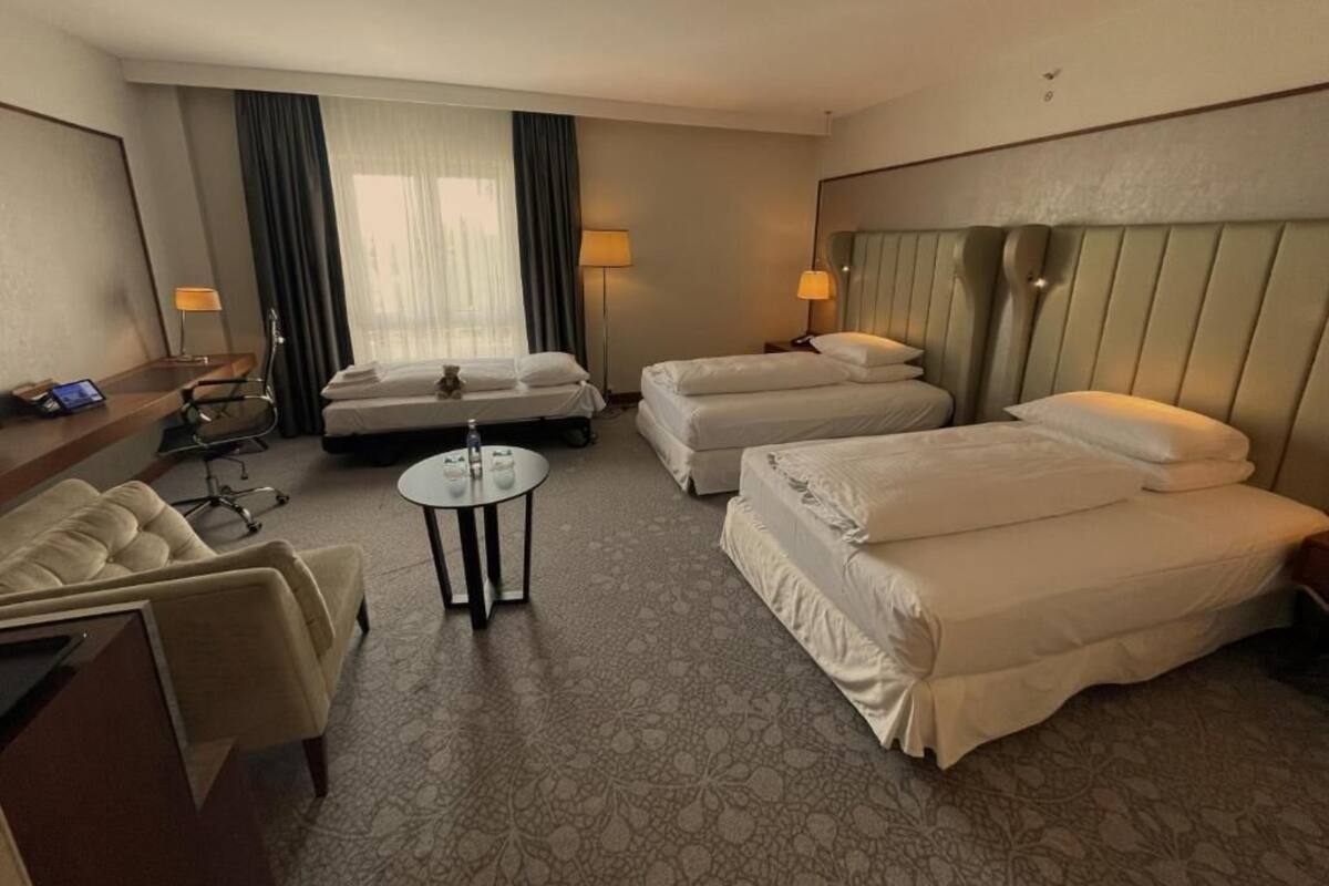 A hotel room with two single beds, a sofa, a small table, and a desk with a chair.